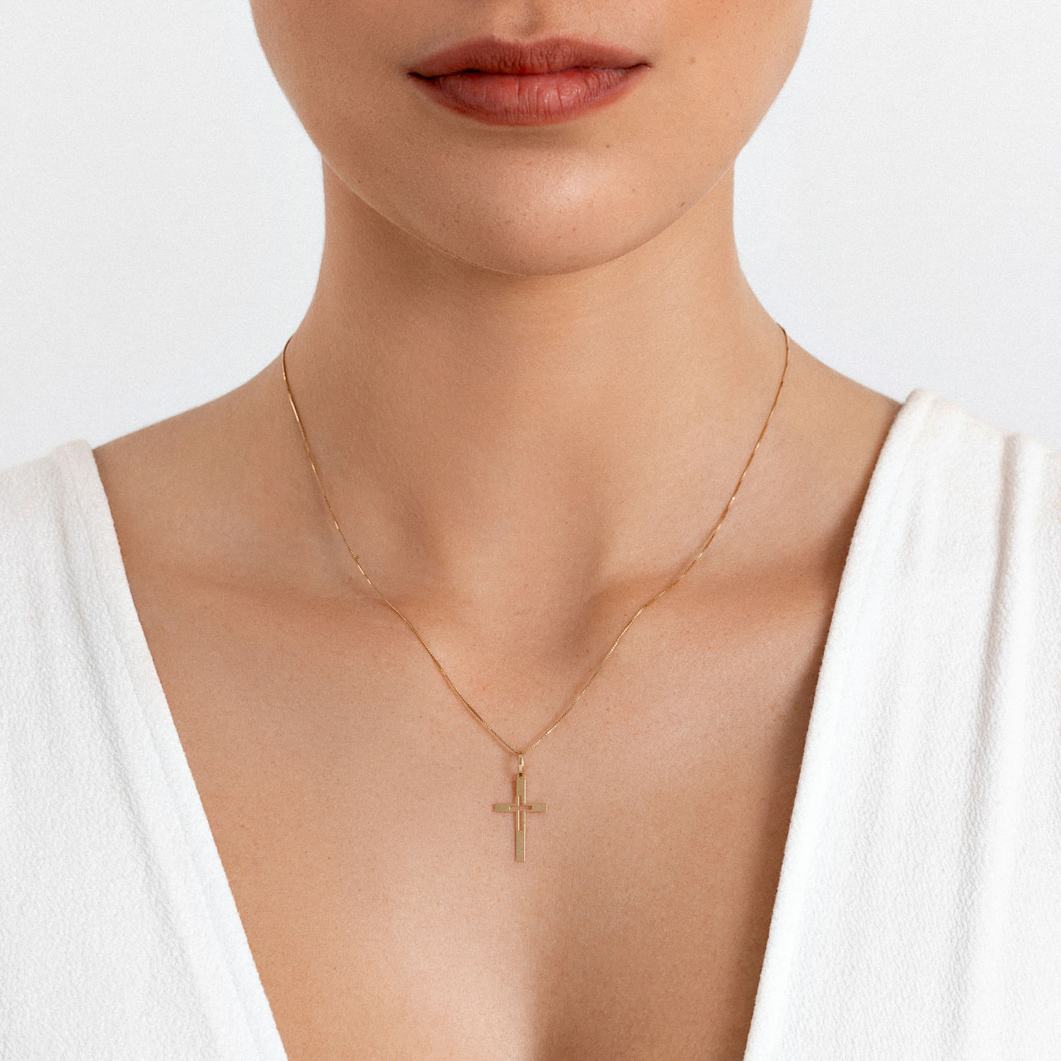 Close-up da boca e pescoço de uma mulher usando uma corrente fina com um colar de cruz dourado.