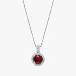 Corrente de prata com pingente circular com pedra vermelha central e detalhes de pedras pequenas ao redor.