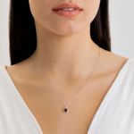 Colar delicado com pingente circular com pedra roxa escura, usando uma blusa branca e cabelo escuro ao fundo.