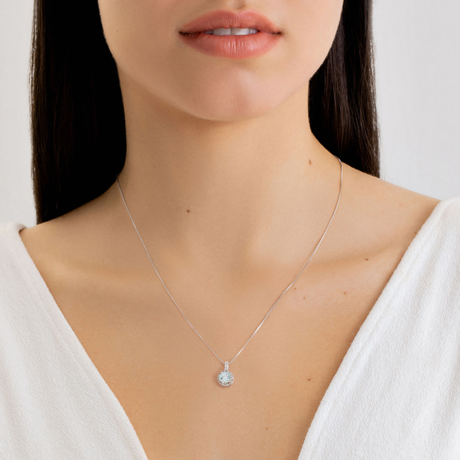 Colar delicado com pingente redondo de pedra ou cristal, usado por uma mulher com blusa branca.