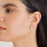 Par de brincos de argola com pedra grande e brilhante, elegantes e prateados, usado na orelha de uma mulher com cabelo escuro.