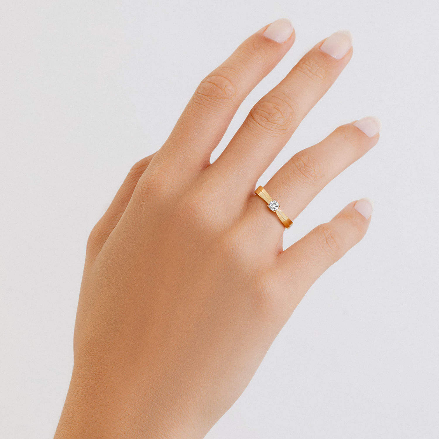 Mão com dedo indicador, médio e anelar visíveis, usando um anel dourado com uma pedra brilhante na ponta do dedo anelar.
