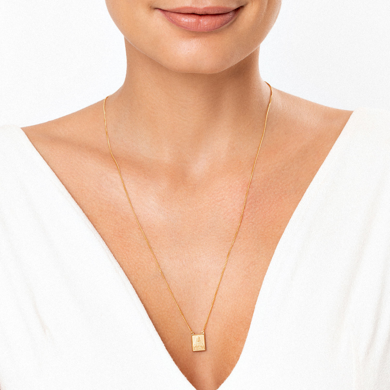 Colar dourado com pingente retangular simples, usado por uma mulher com blusa branca e pele clara.