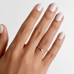 Dedo com unhas bem cuidadas usando esmalte branco e anel de noivado com uma pedra central grande e pequenas pedras ao redor.