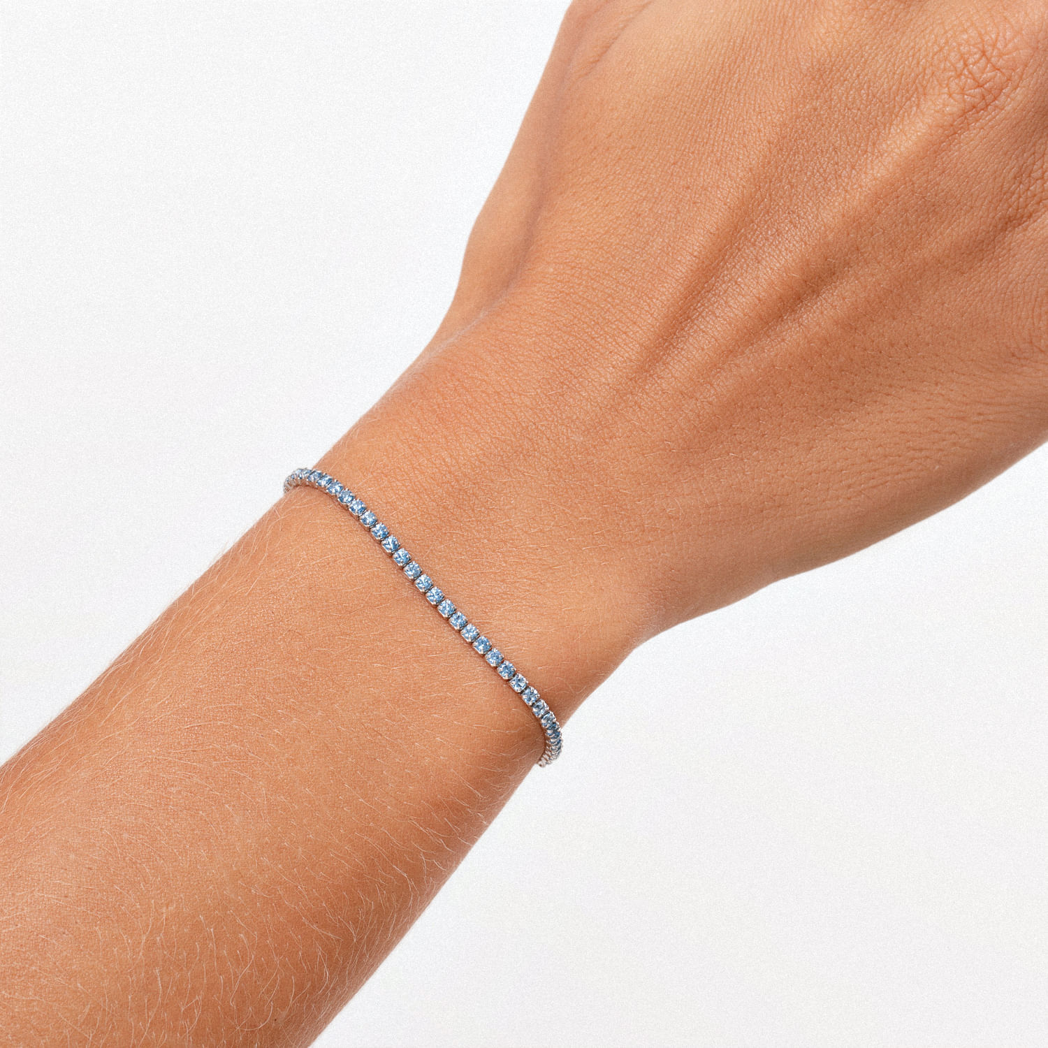 Pulseira com pedras azuis finas e brilhantes no pulso de uma mão com pele clara.