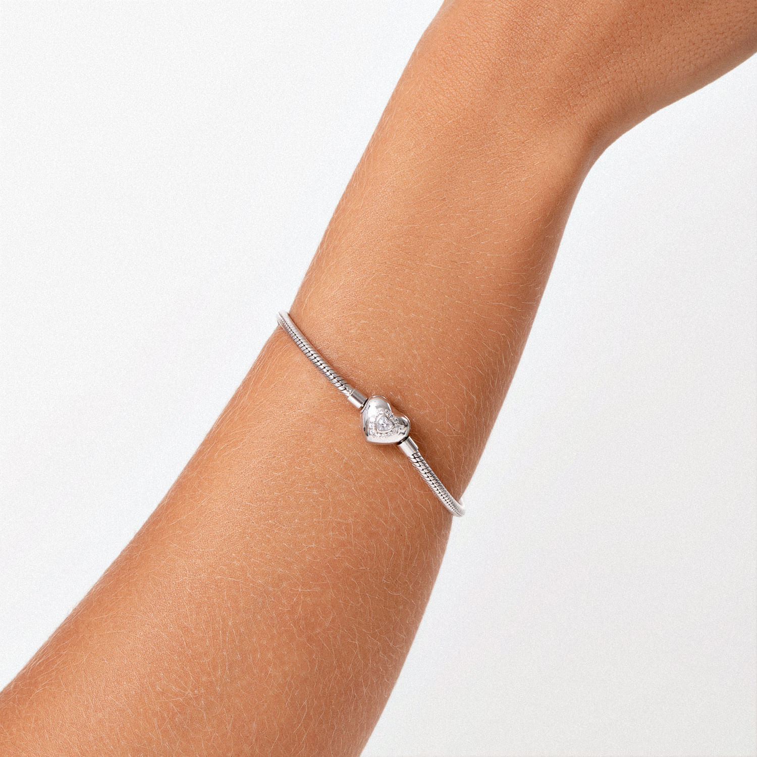Pulseira prateada com coração decorado, usada no pulso de uma pessoa.