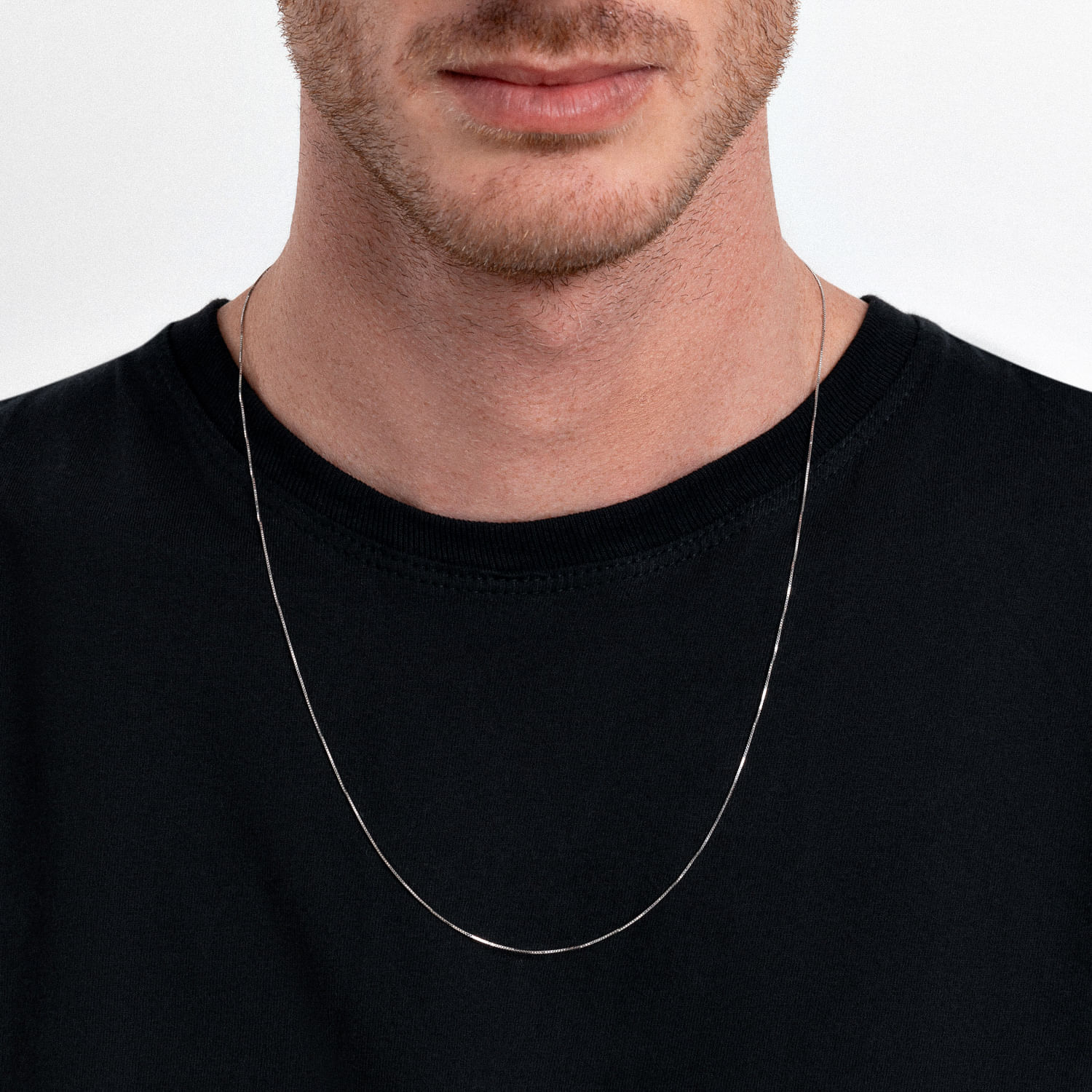 Homem usando uma camiseta preta e uma corrente fina de prata ao redor do pescoço.