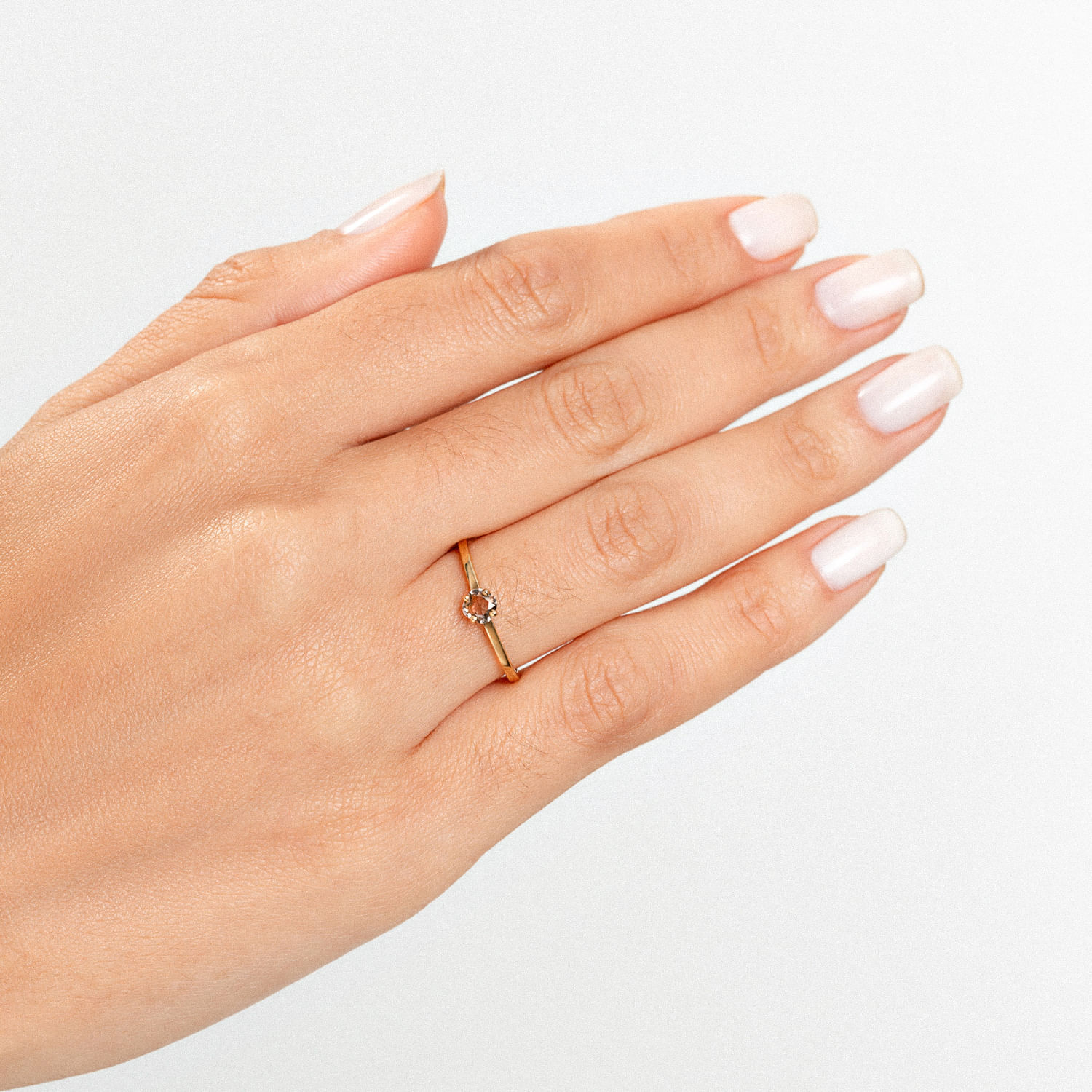 Mão com unhas brancas usando um anel dourado com uma pedra no centro.