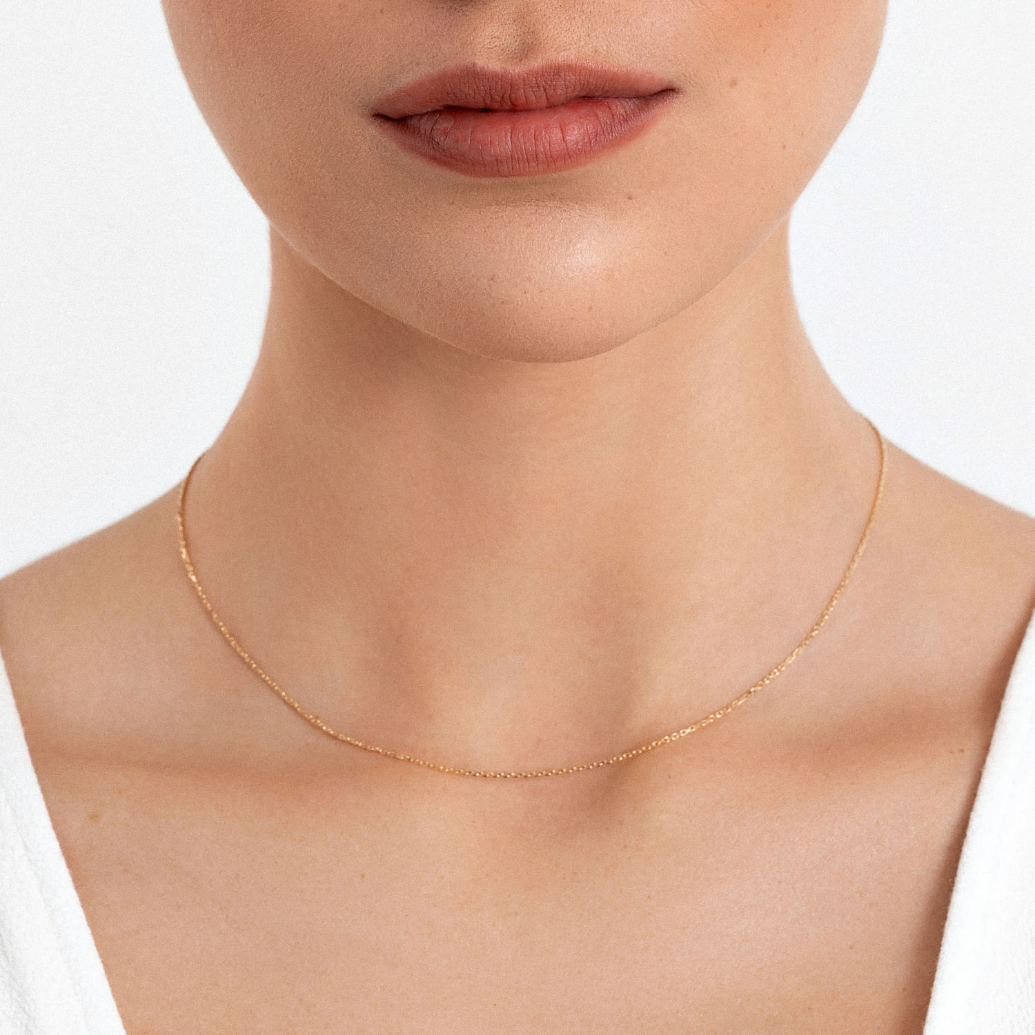 Colar delicado dourado com pingente de pequenas bolinhas, usado por uma mulher com pele clara e lábios rosados.