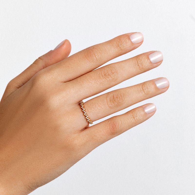 Dedo com unha esmalte clara e anel delicado com pequenas pedras dourado na mão esquerda.