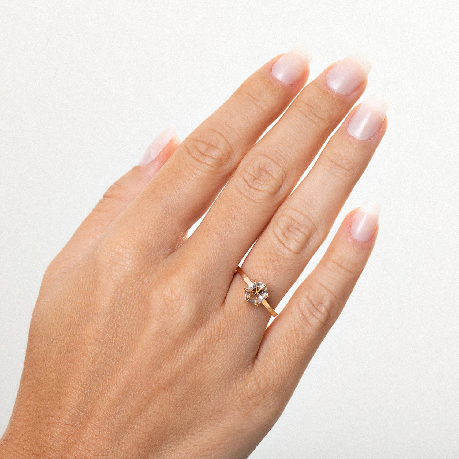 Dedo feminino com unha bem cuidada usando anel com pedra brilhante em fundo branco.