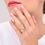 Dedo de uma mulher com unhas bem cuidadas usando um anel dourado com detalhes prateados, perto do rosto com batom cor de rosa.