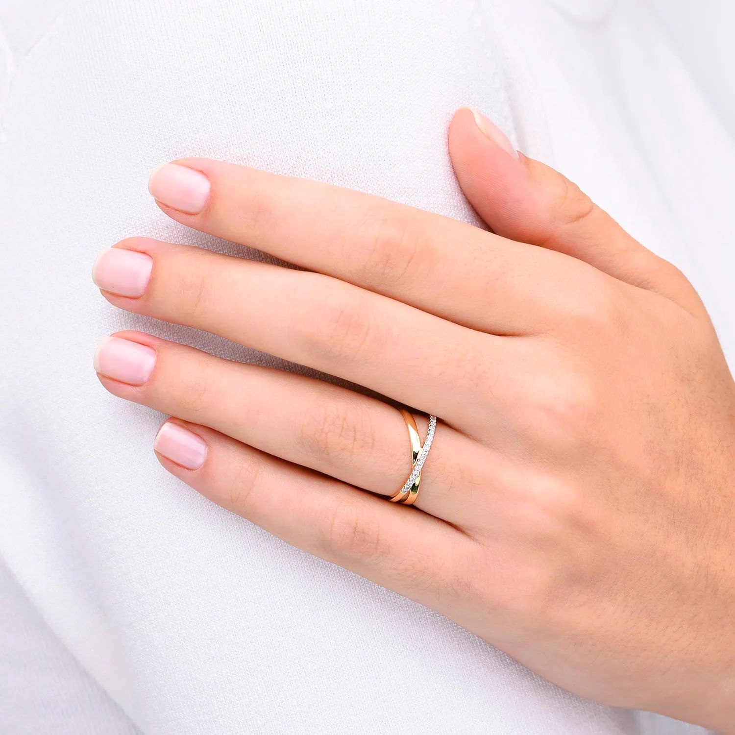 Mão com unhas neatly manicured, usando um anel dourado com detalhes em pedra branca, sobre fundo branco.