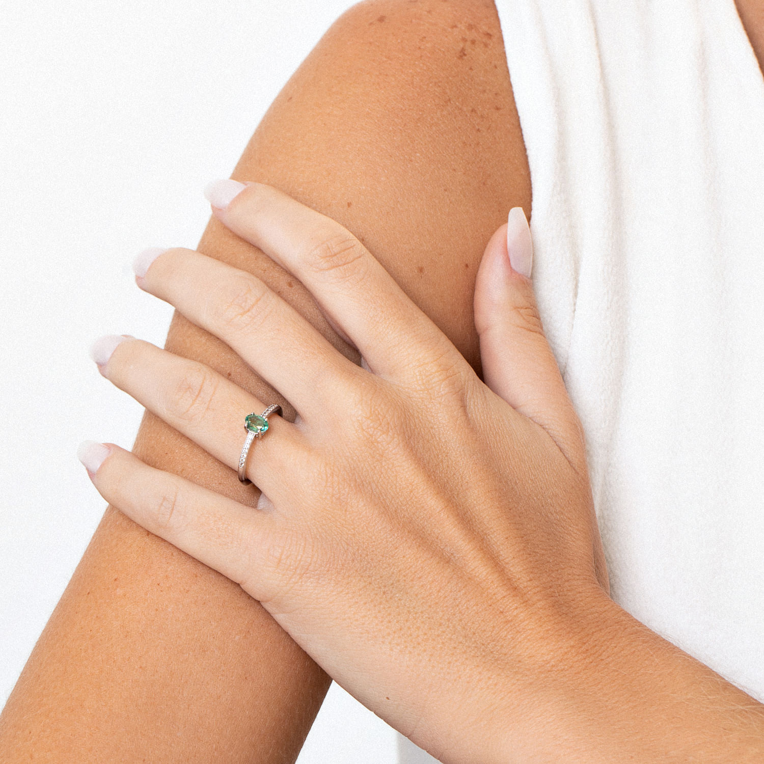 Mano com esmalte claro e anel com pedra verde, repousando sobre o braço.