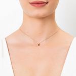 Colar delicado de corrente dourada com pingente pequeno negro, usado por uma pessoa com pele clara e vestido branco.