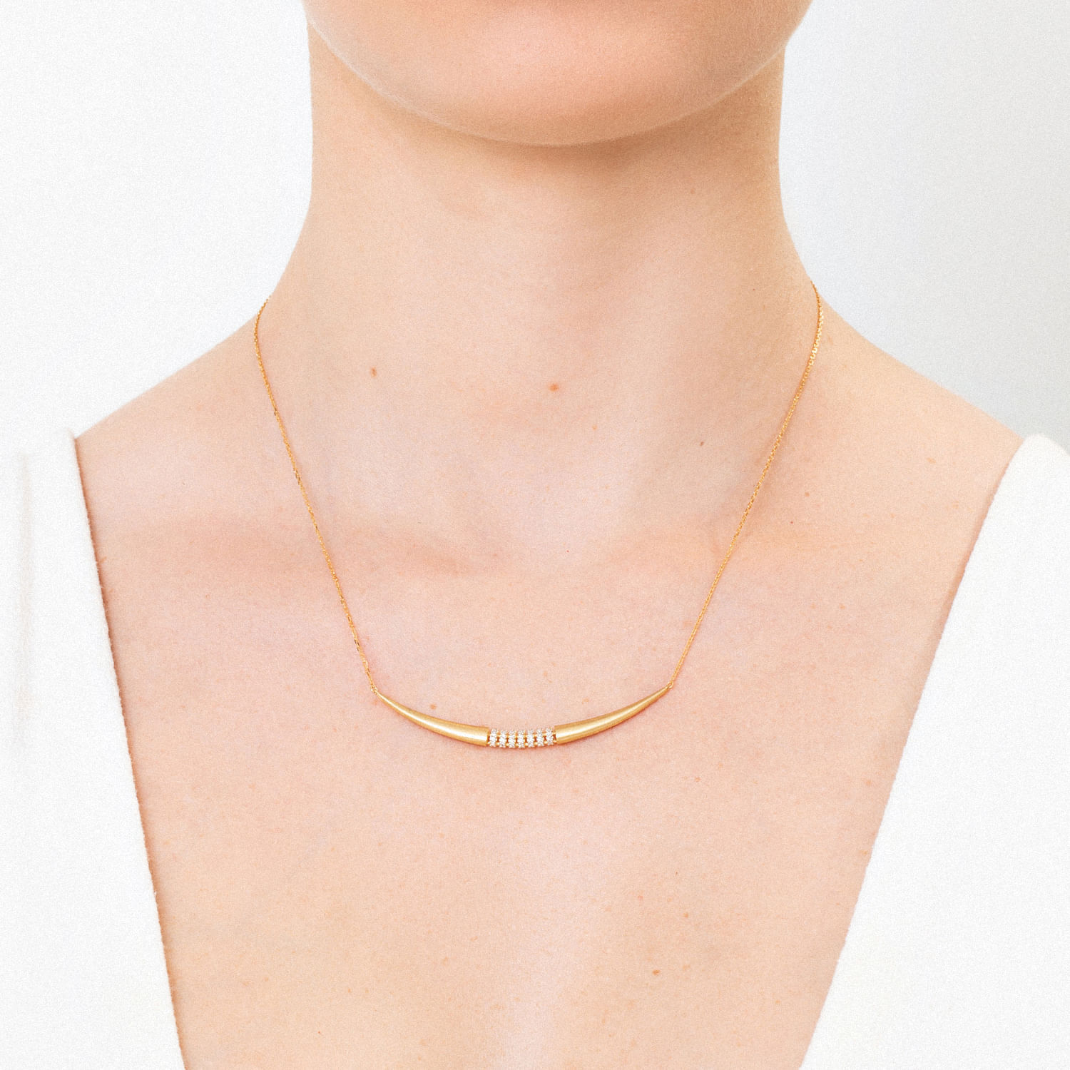 Colar dourado com pingente curvo e detalhes de pequenas pedras, em torno do pescoço de uma mulher.