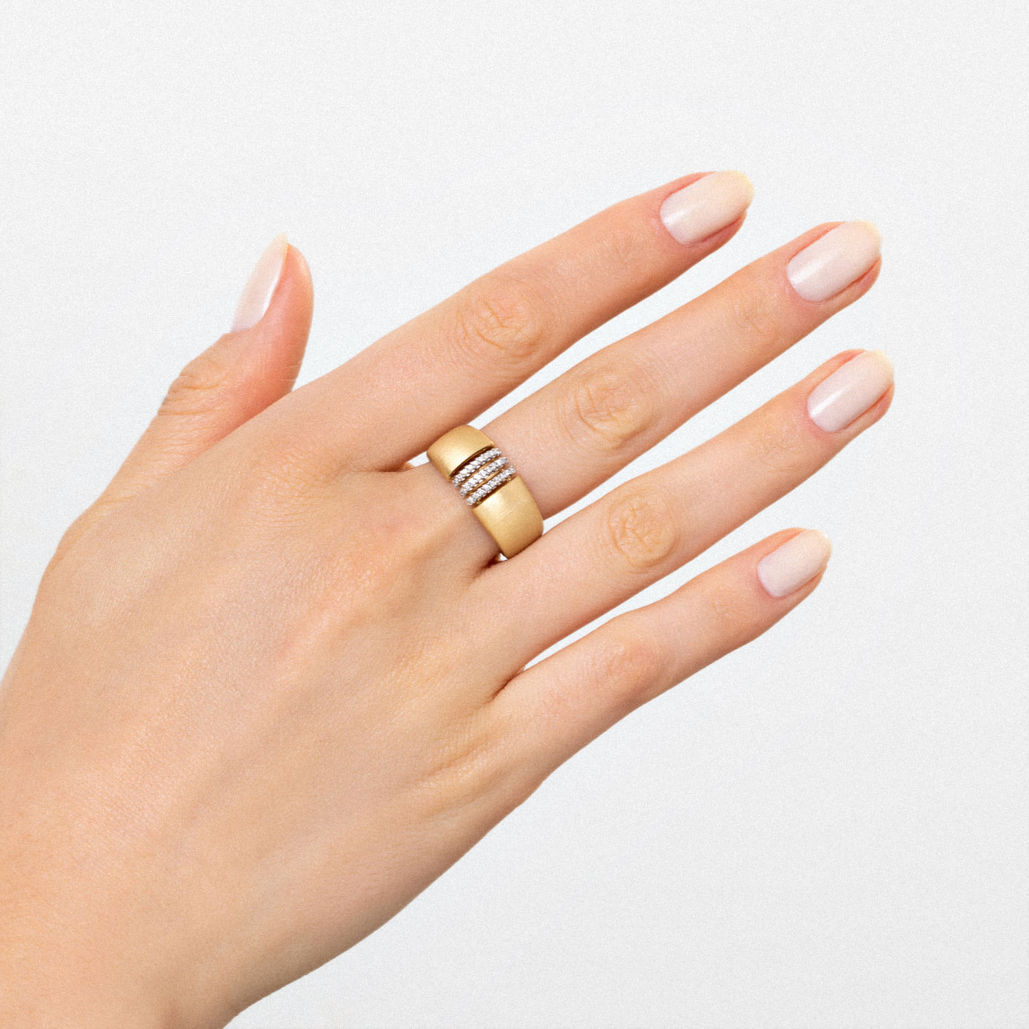 Mão com unhas pintadas de branco usando um anel dourado com detalhes de pedras no dedo médio.