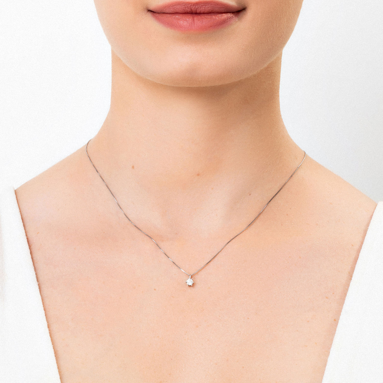 Colar delicado com pingente de diamante em volta de uma pessoa com pele clara, usando blusa branca.