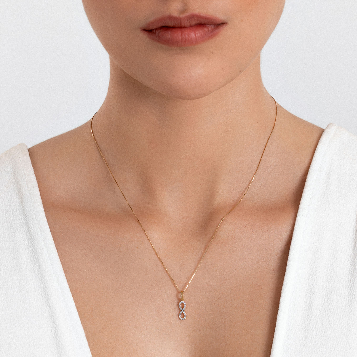Colar feminino de corrente fina com pingente de dois círculos entrelaçados, em tom dourado, usado por uma mulher com blusa branca.