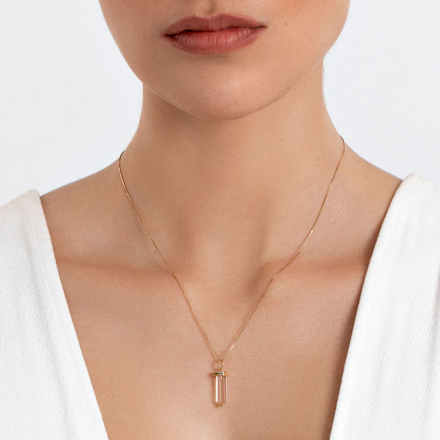 Colar dourado com pingente de cristal translúcido em forma de bastão, em destaque na imagem.