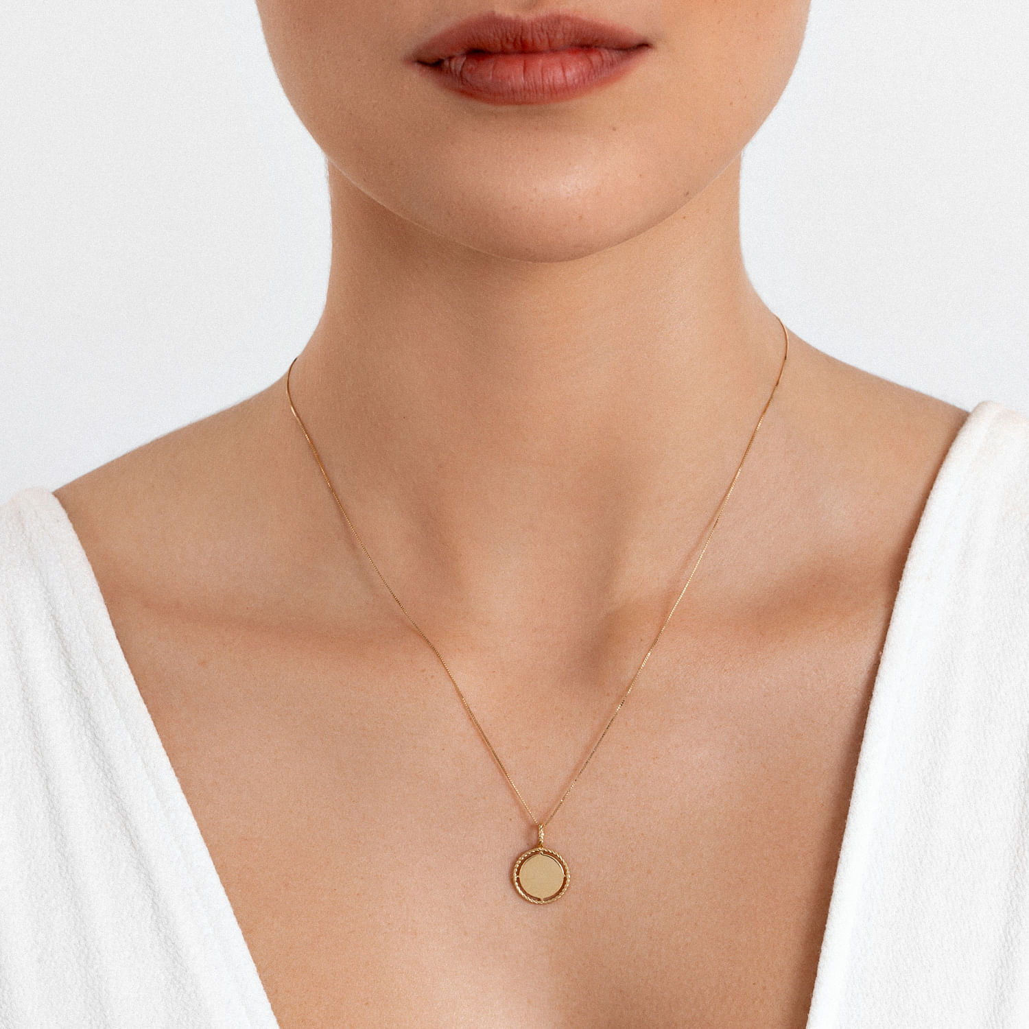 Colar dourado com pingente circular simples, usado por uma pessoa com blusa branca.