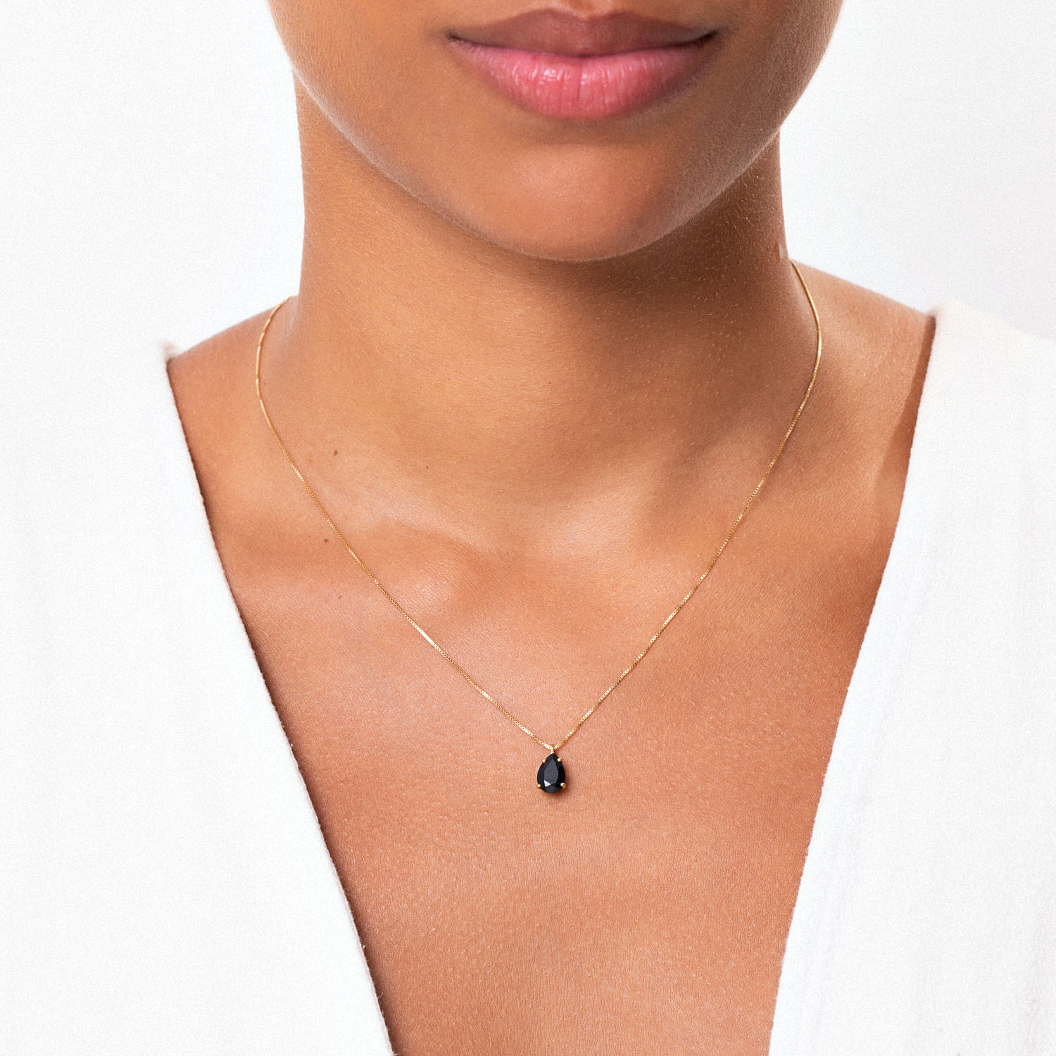 Colar delicado de corrente fina com pingente preto em formato de gota, usado por uma mulher com pele morena e lábios rosados.