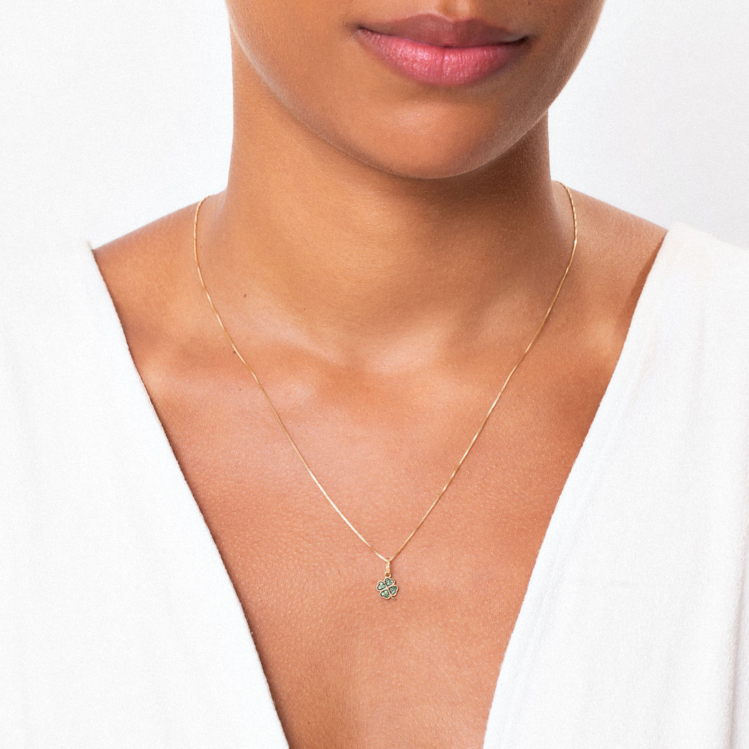 Colar delicado de ouro com pingente de flor com pedras, usado por uma mulher com pele morena e camiseta branca.