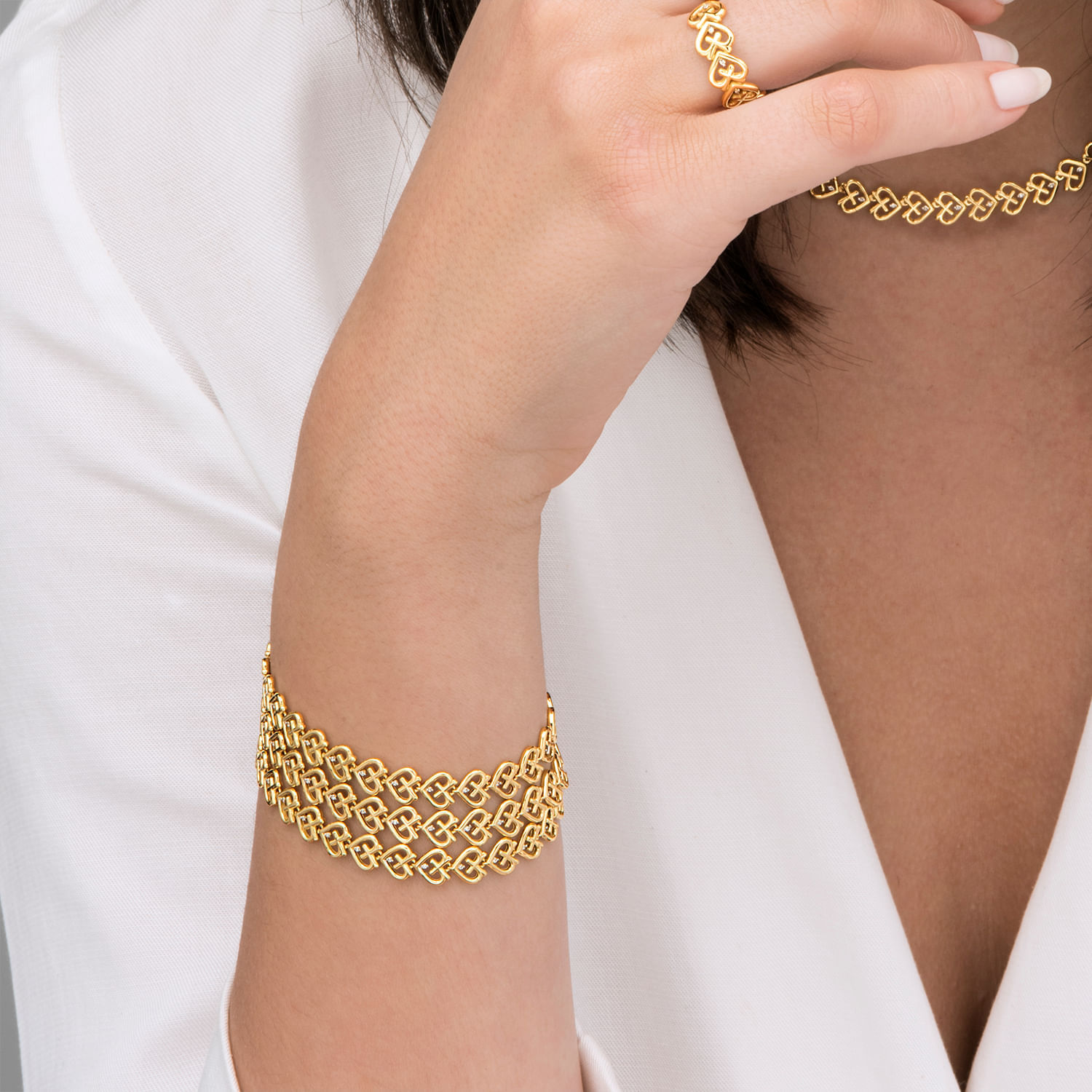 Conjunto de joias douradas, incluindo uma pulseira, anel e colar, com design de elos interligados.