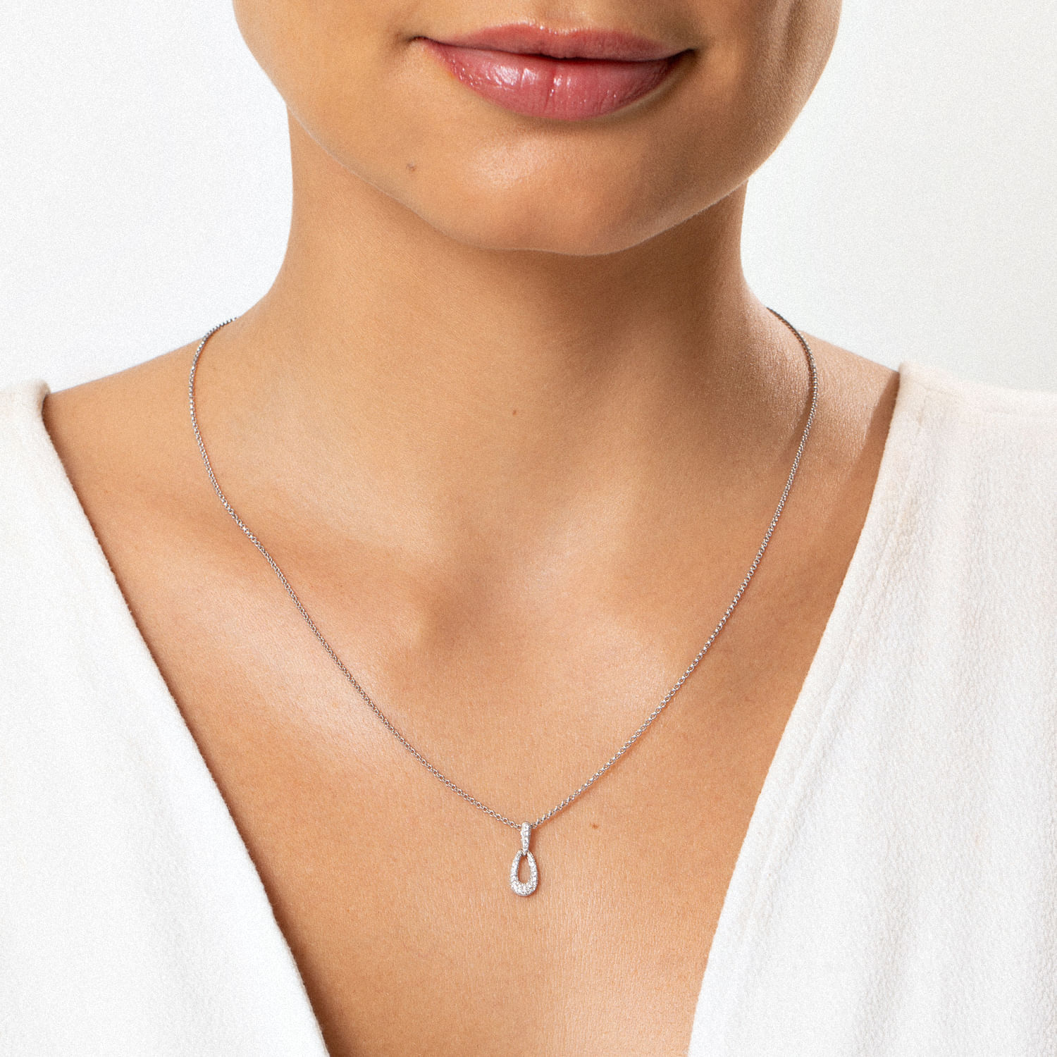 Colar delicado com pingente de gota com pedras, usado por uma mulher com blusa branca.