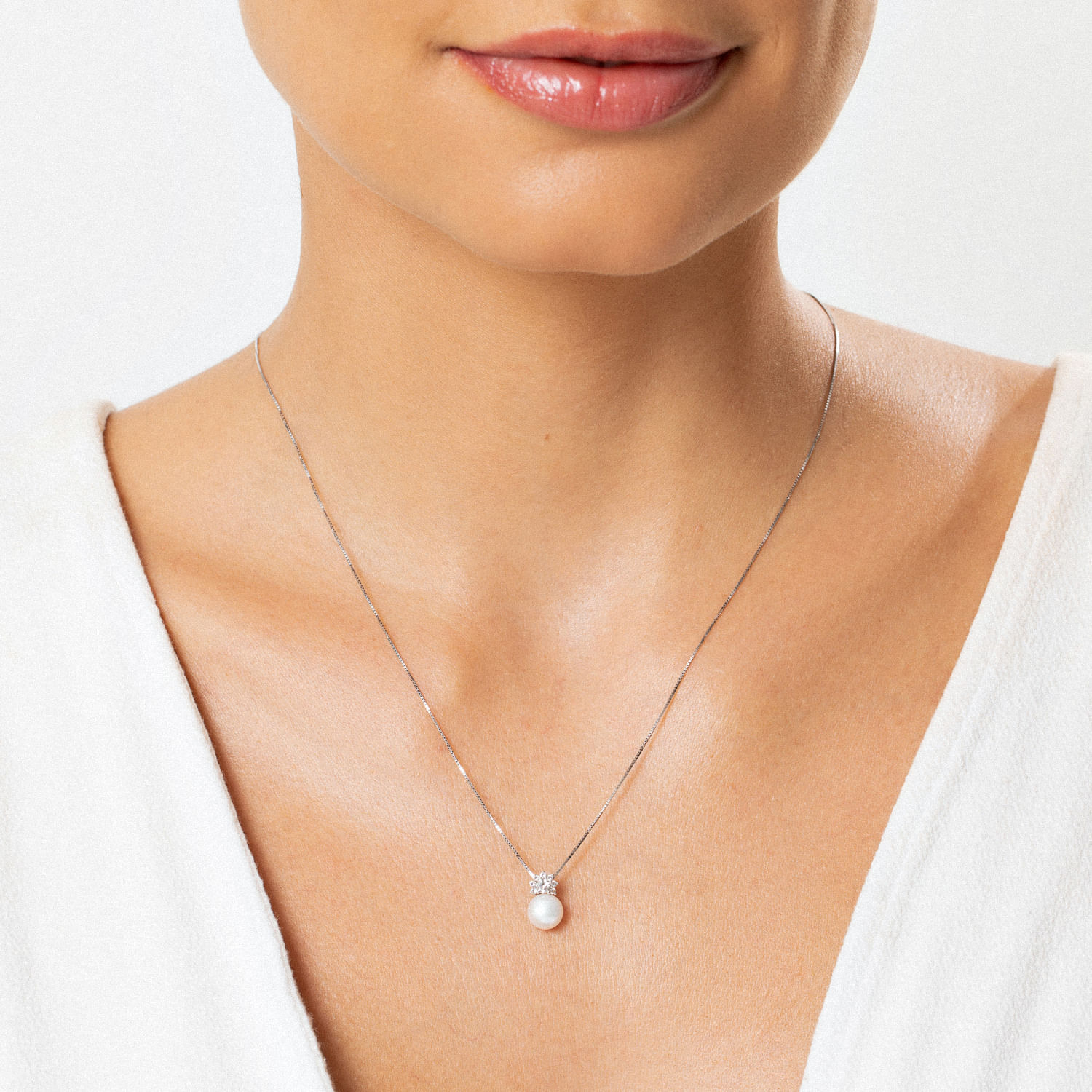 Colar com pingente de pérola e detalhes em prata, usado por uma mulher com blusa branca.