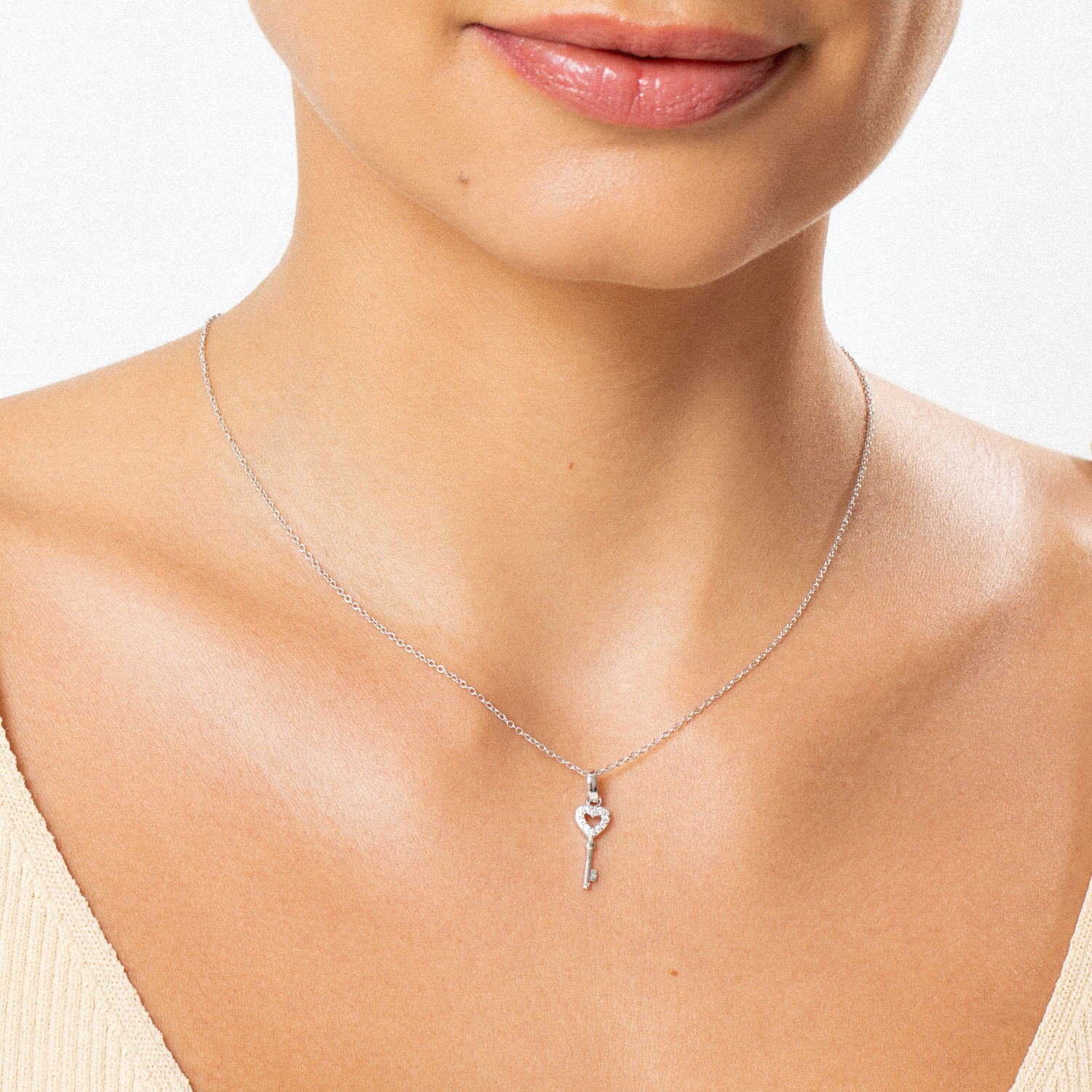 Colar com pingente em forma de chave, feito de metal prateado com detalhes brilhantes, usado na base do pescoço de uma mulher.