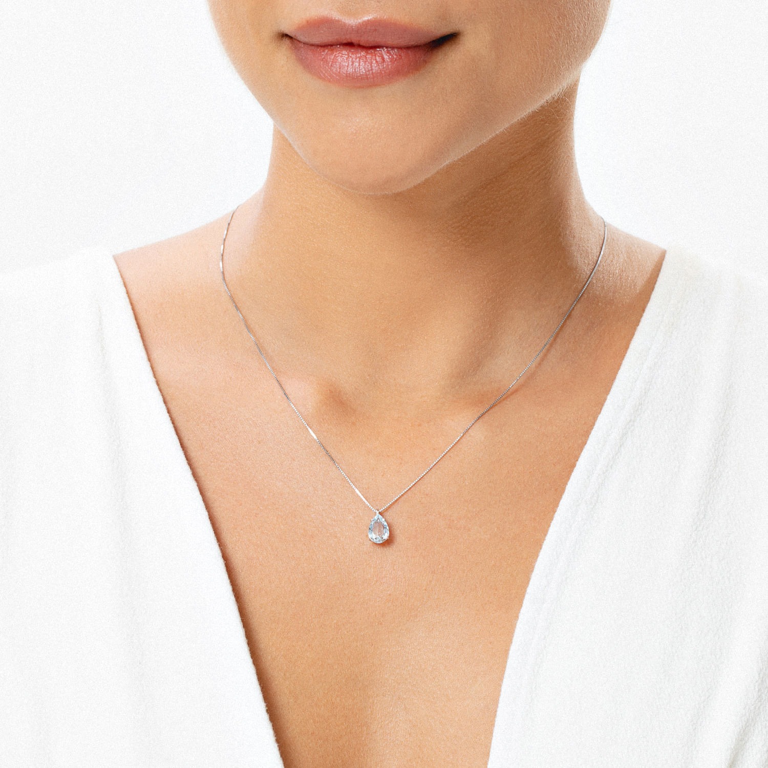 Colar de prata com pingente de gota com pedra brilhante, usado por uma mulher com blusa branca.