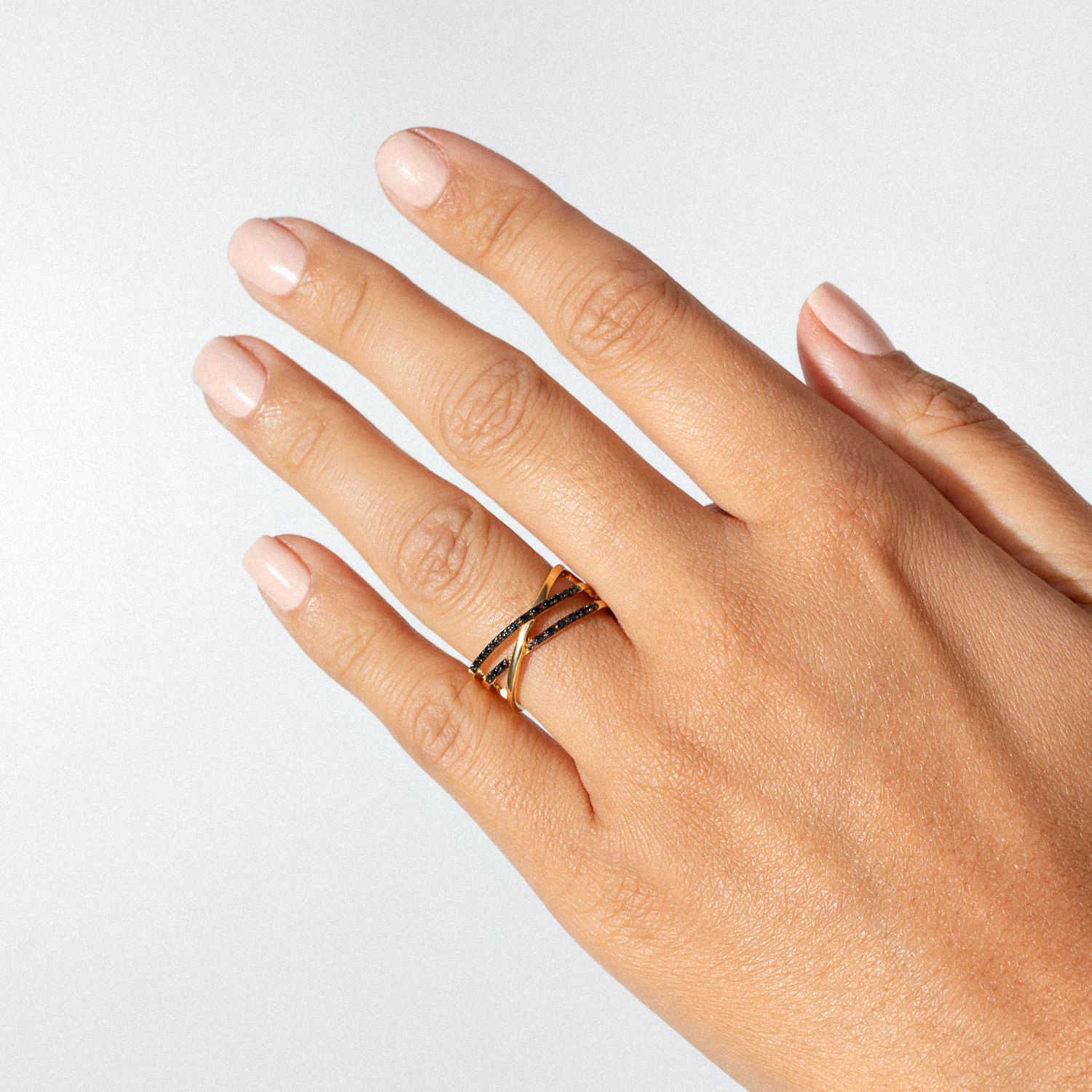 Mão com unhas lixadas e polidas, usando duas alianças douradas com detalhes pretos, sobre fundo branco.