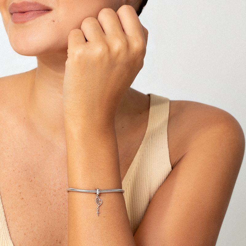 Pingente de prata com coração, símbolo de infinito e cruz pendurados.