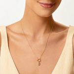 Colar dourado com pingente oval com detalhes internos, usado por uma pessoa com camiseta branca.