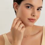 Mulher usando brincos, colar e anel dourados com detalhes brilhantes, em um fundo claro.