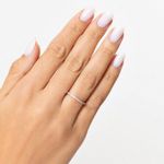 Dedo com unha unhas pintadas de branco, usando um anel delicado com pedras brilhantes em um dedo.