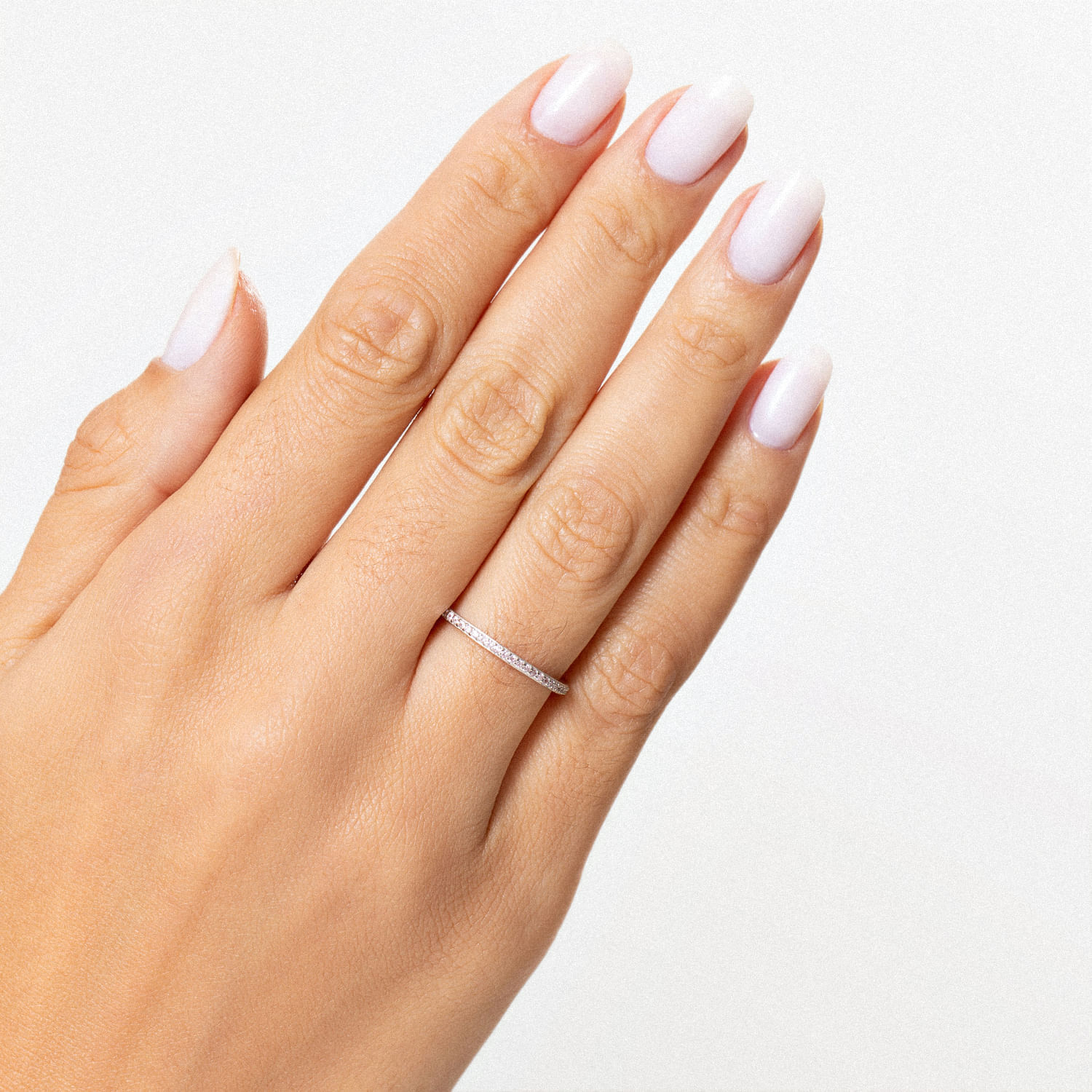 Dedo com unha unhas pintadas de branco, usando um anel delicado com pedras brilhantes em um dedo.